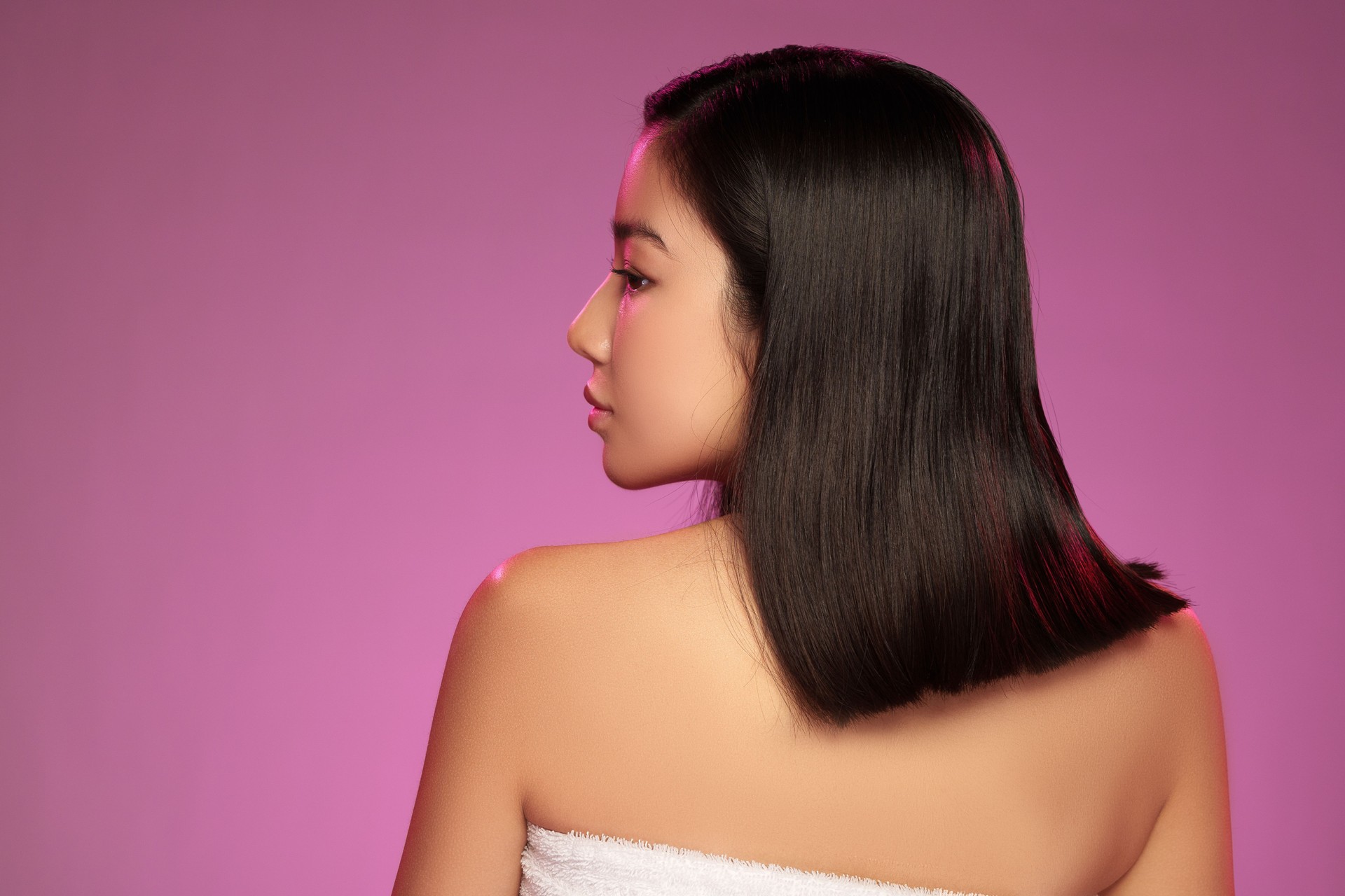 Stylish young woman with sleek hair poses against a vibrant pink background in a creative setting
