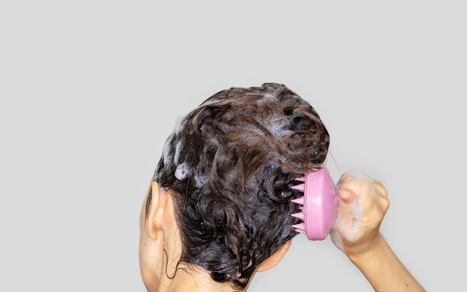 woman using silicone pink shampoo brush for scalp massage hair growth stimulation isolated